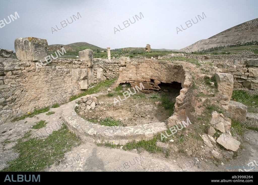 The House of the Hunt, Bulla Regia, Tunisia. The House of the Hunt, which takes its name from a mosaic in the basement, evidently belonged to a wealthy citizen. It was constructed by combining and altering a number of small existing houses. The upper floor is badly ruined, but the basement, lying some 5m (16ft) below ground level, is well preserved. The rooms, laid out round a courtyard lined with Corinthian columns, include bedrooms (identified by the small mosaic-decorated platforms for the beds) and a large dining room (triclinium), also with a pavement mosaic. The bedrooms have an interesting air supply and ventilation system, with pipes built into the walls which communicate with an air shaft surrounding the rooms. The layout on the ground floor is similar, with two colonnaded courtyards, dining and living rooms, bedrooms and a small bath-house. Bulla Regia is an archaeological site in northwestern Tunisia, a former Roman city near modern Jendouba. It is noted for its Hadrianic-era semi-subterranean housing, a protection from the fierce heat and effects of the sun.