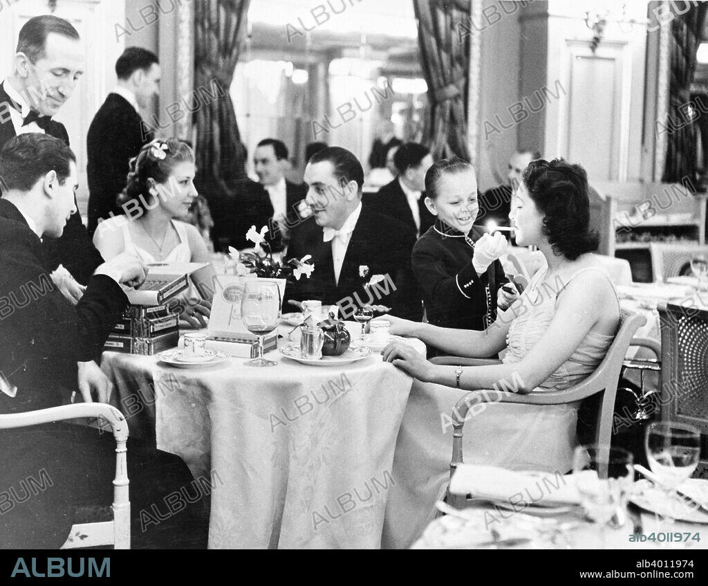 People dining at the Trocadero Restaurant, Leicester Square, Westminster, London, 1939. A young boy wearing gloves lights a woman's cigarette. The elegant restaurant, near Piccadilly Circus, opened in 1896.
