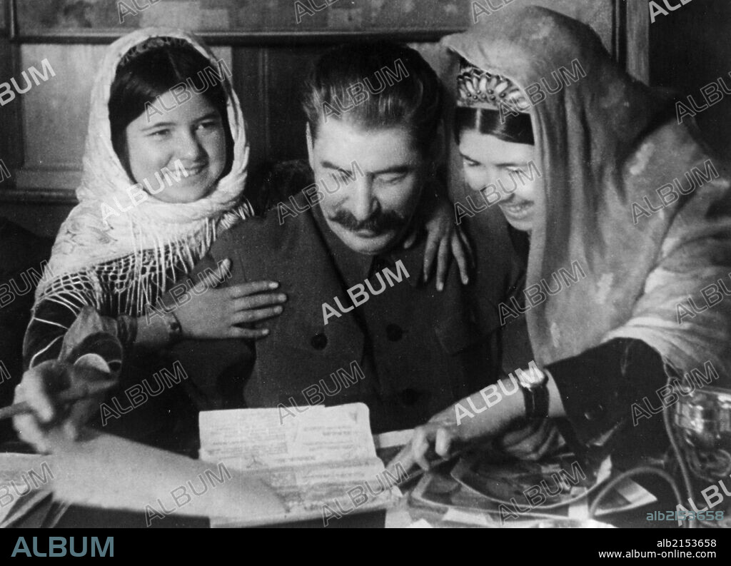 Joseph stalin with two young women from a collective farm in tadjikistan at a conference on cotton farming, january 1935.