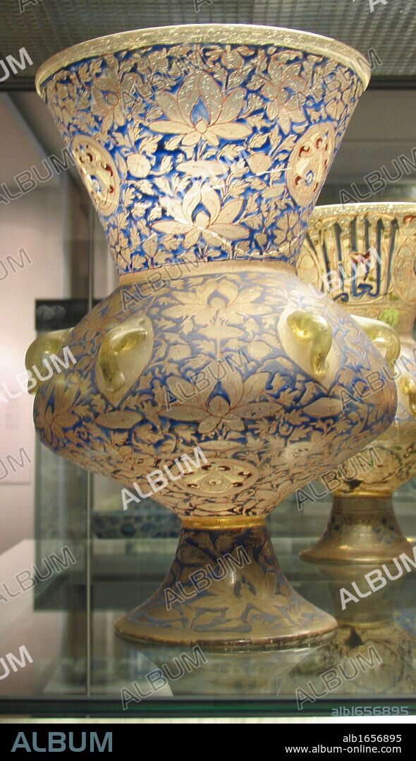 Mosque lamp. Mamluk dynasty, about AD 1350-55 From Cairo, Egypt. The lamp is also decorated with a bold inscription frieze containing the name and titles of Sayf al-Din Shaykhu al-Nasiri, and his heraldic device incorporating a red cup appears in the centre of the roundels on the neck and the underside of the lamp.