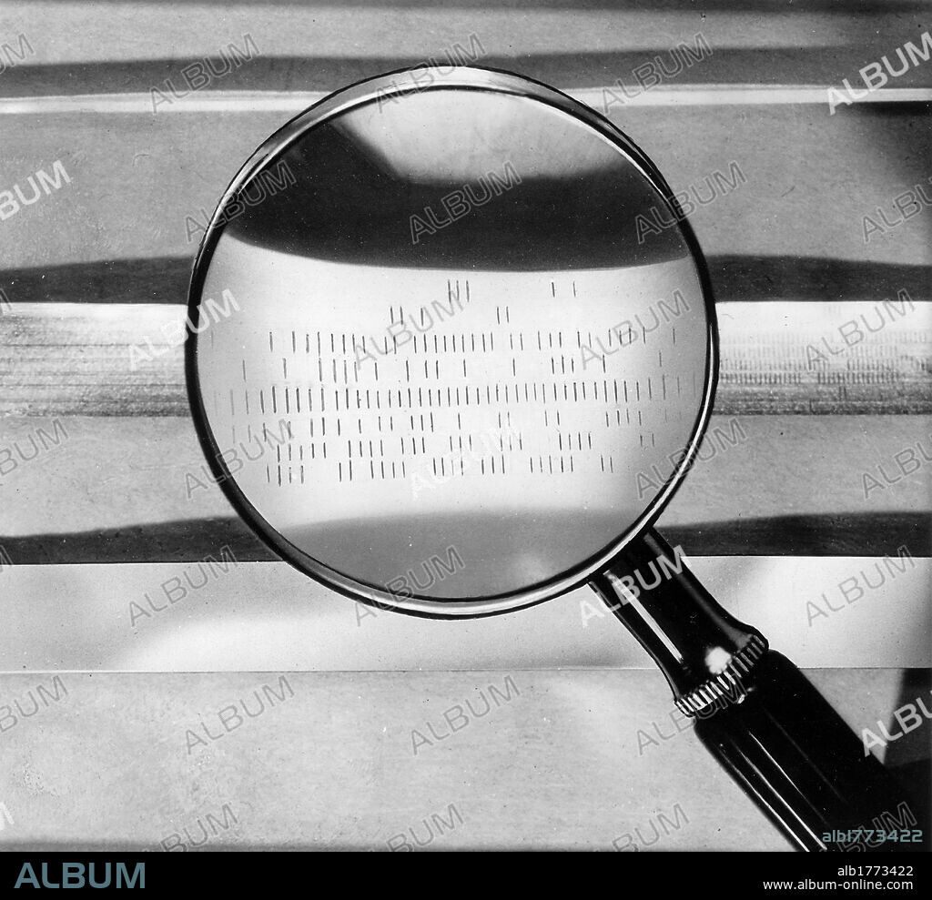 Magnetic tape seen through a magnifying glass. A magnifying glass showing details of an electronic calculator magnetic tape. 1960s.
