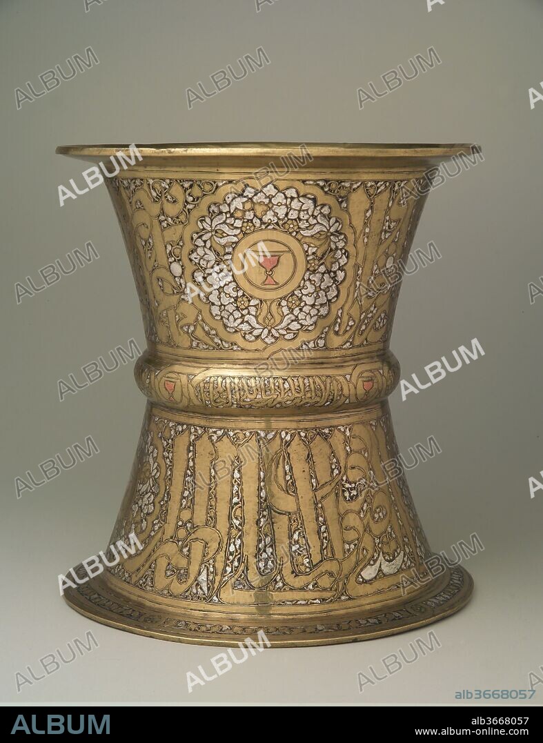 Tray Stand. Dimensions: H. 10 1/4 in. (26.0 cm)
D. 9 5/8 in. (24.4 cm). Date: mid-14th century.
Similar stands were widely employed in the Mamluk period to host large rounded metal trays (such as 91.1.604), on which fruits and other food were displayed.
The cup motif inlaid with copper stands out among the richly decoration of this tray. It was a blazon of the cupbearer, one of the differentiated offices of the court of the Mamluk sultans. The inscription reads Husain, son of Qawsun, who was cupbearer to Muhammad b. Qalawun (al-Malik al-Nasir) (1294-1340/41). Despite having been ousted after the sultan's death, Qawsun's prestige must have endured, as his sons continued to use his emblem of the ringed cup set within a divided shield.
The glass mosque lamp 17.190.991 was also made for him, as indicated by its inscription.