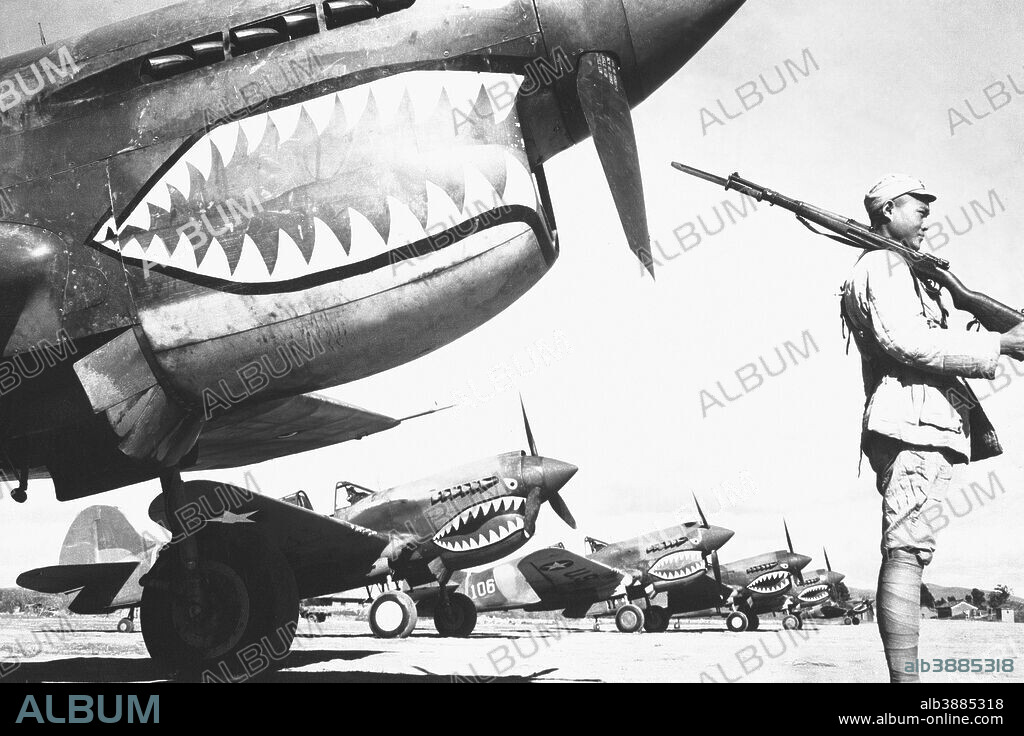 A Chinese soldier guards a line of American P-40 fighter planes, painted with the shark-face emblem of the Flying Tigers, at a flying field somewhere in China. The American pursuit planes have a 12-to-1 victory ratio over the Japanese. Ca. 1942.