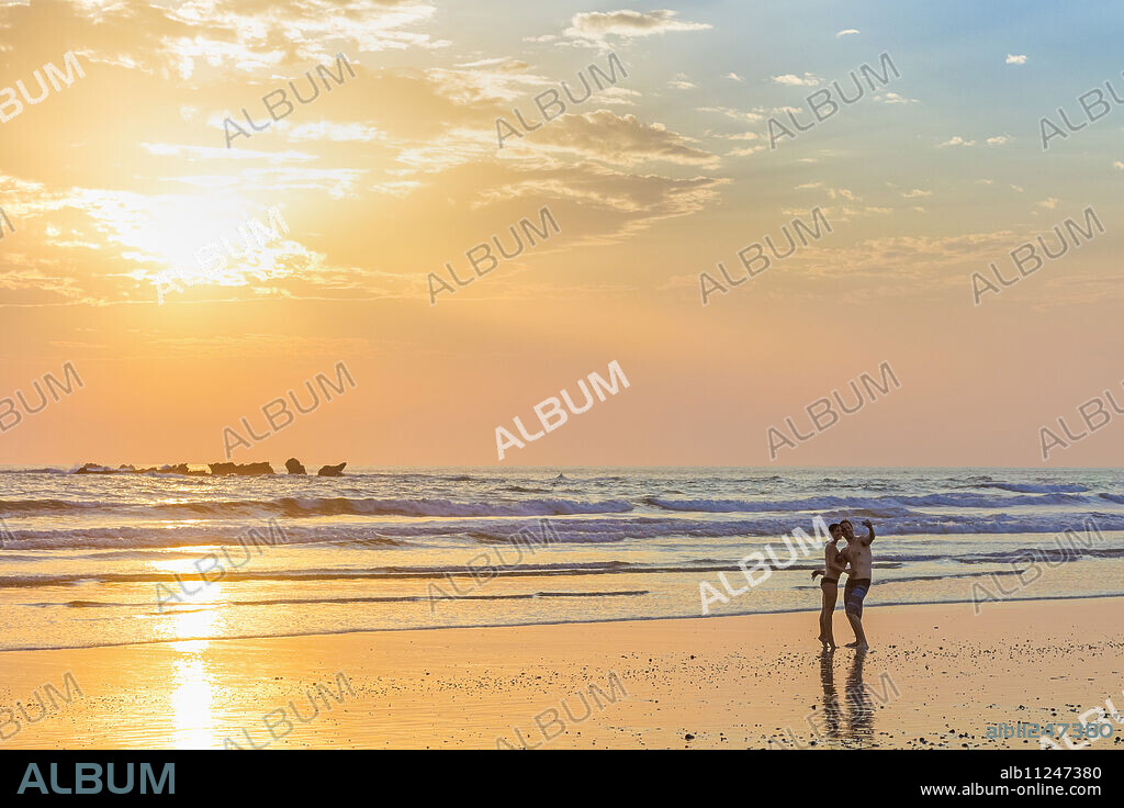 Couple photographing themselves at sunset, Playa Guiones surf beach, Nosara, Nicoya Peninsula, Guanacaste Province, Costa Rica, Central America.