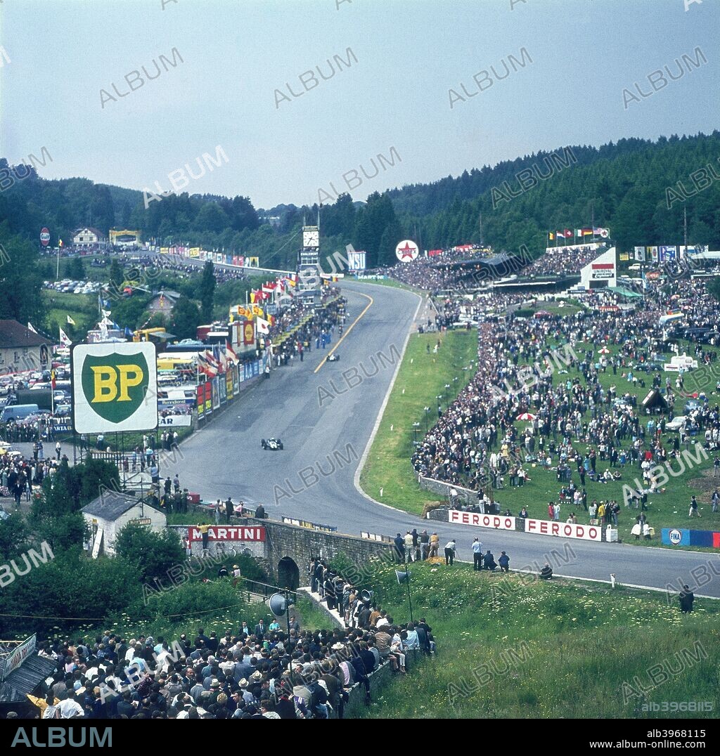 Part of Spa-Francorchamps race track, Belgian Grand Prix, Belgium, 1963. Spectators line either side of this part of the course as two racing cars can be seen approaching the bend.
