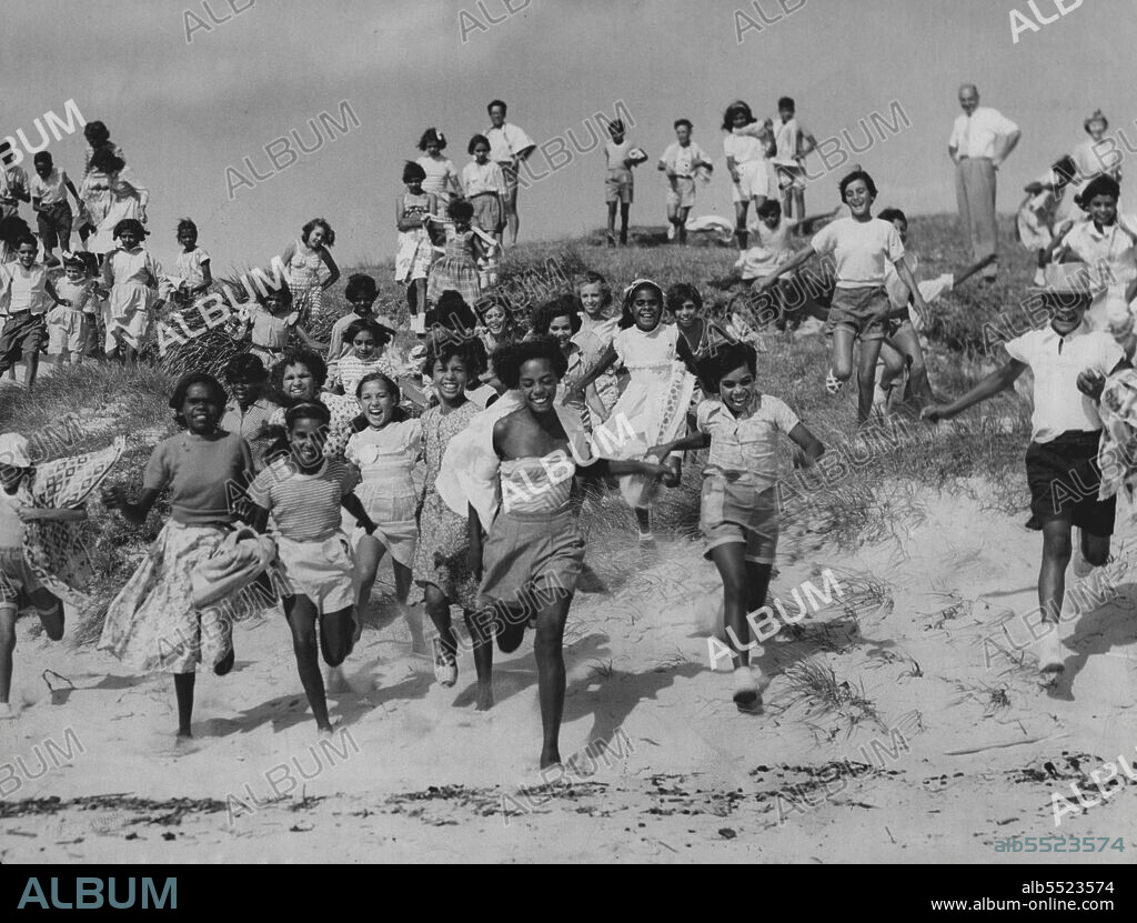 City Holiday For Abo Children -- Some of the 70 aboriginal children from the far west who have been brought to Sydney for 2 weeks holiday by the Aboriginal welfare board, racing down fro their first Dip at La Perouse to-day. It was the first time most of them had seen the sea. Some of the children came 900 mile for their holiday. Ages range from 9 to 13 years. January 9, 1955. (Photo by Ronald Leslie Stewart/Fairfax Media).