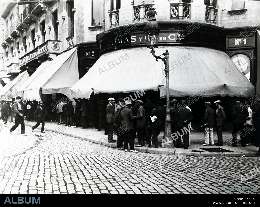 Barcelona. Establecimiento Comas y Cia. en comandita, camisería y sombrerería situada en la Ronda de San Pedro esquina con el Paseo de Gracia. Grupos de hombres dirigiéndose por el paseo de Gracia, presumiblemente, a un acto político o deportivo en el cercano salón Novedades de la calle de Caspe. Años 1915.