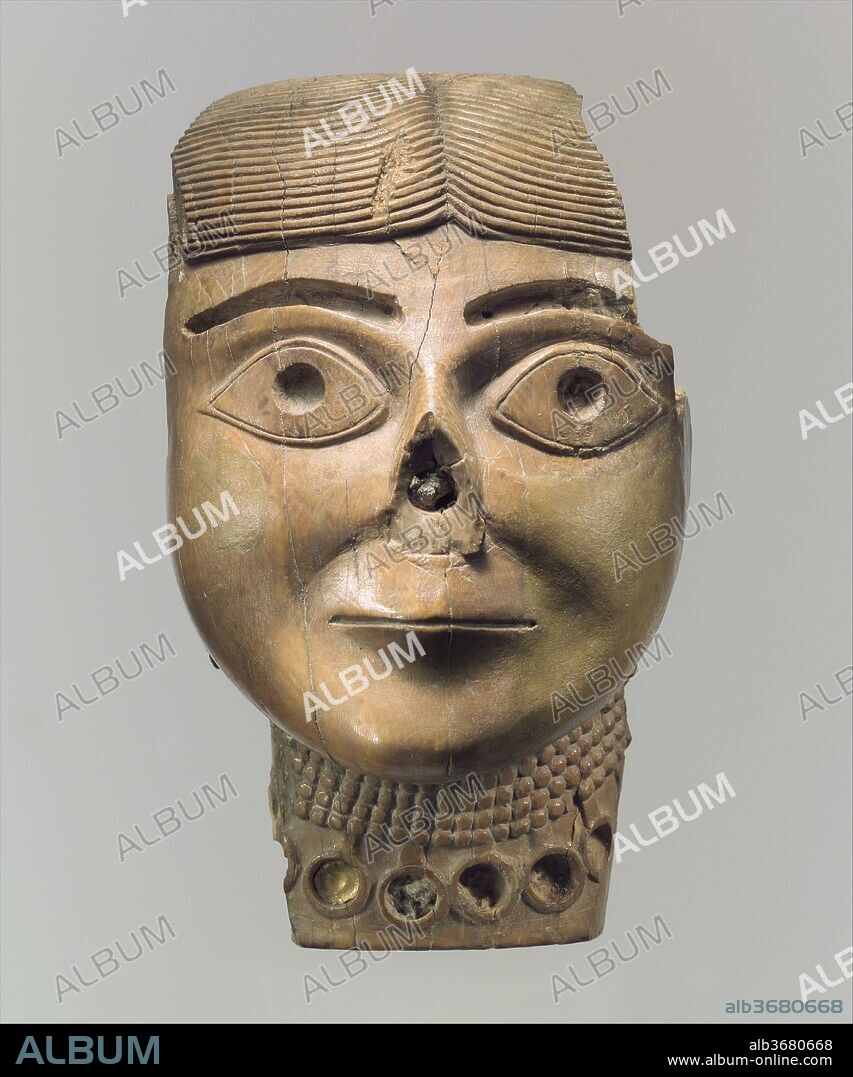 Head of a female wearing a necklace originally filled with stone inlay and gold. Culture: Assyrian. Dimensions: 5.39 x 3.27 in. (13.69 x 8.31 cm). Date: ca. 9th-8th century B.C..
This female head was found in a well in the Northwest Palace of Ashurnasirpal, and its warm color is a result of long exposure to the well water or sludge. It is one of the two largest ivory heads known from the ancient Near East. The other, from the same well, is now in the Iraq Museum in Baghdad. The ivory heads were thrown in the well when the palace was sacked, perhaps during the final defeat of Assyria at the end of the seventh century B.C. Originally, they may have been part of statues made from various materials, including gold, wood, and textiles, which are recorded in texts but have not survived intact. Two mortises (square-ended recesses) were cut into the flat rear surface of the ivory for the attachment of separate elements above and below. A small piece of gold inlay survives in the choker-style necklace, and the cavities marking the eyebrows and pupils, now empty, must have been inlaid in contrasting materials as well. The fleshy cheeks and chin are softly modeled, in a striking counterpoint to the otherwise stylized features of the ridged hair, large, staring eyes, and thin mouth set in a line. Broken in antiquity, the nose was repaired by a separate piece attached with a dowel, now missing and revealing a prominent socket. The figure's features resemble those of Syrian style ivories, which are characterized by large eyes, small chins and full cheeks. Like these Syrian ivories, the nose was probably intended to be quite prominent. It is not known whether the head depicts a woman--perhaps a royal or religious figure--or a deity.
Built by the Assyrian king Ashurnasirpal II, the palaces and storerooms of Nimrud housed thousands of pieces of carved ivory. Most of the ivories served as furniture inlays or small precious objects such as boxes. While some of them were carved in the same style as the large Assyrian reliefs lining the walls of the Northwest Palace, the majority of the ivories display images and styles related to the arts of North Syria and the Phoenician city-states. Phoenician style ivories are distinguished by their use of imagery related to Egyptian art, such as sphinxes and figures wearing pharaonic crowns, and the use of elaborate carving techniques such as openwork and colored glass inlay. North Syrian style ivories tend to depict stockier figures in more dynamic compositions, carved as solid plaques with fewer added decorative elements. However, some pieces do not fit easily into any of these three styles. Most of the ivories were probably collected by the Assyrian kings as tribute from vassal states, and as booty from conquered enemies, while some may have been manufactured in workshops at Nimrud. The ivory tusks that provided the raw material for these objects were almost certainly from African elephants, imported from lands south of Egypt, although elephants did inhabit several river valleys in Syria until they were hunted to extinction by the end of the eighth century B.C.