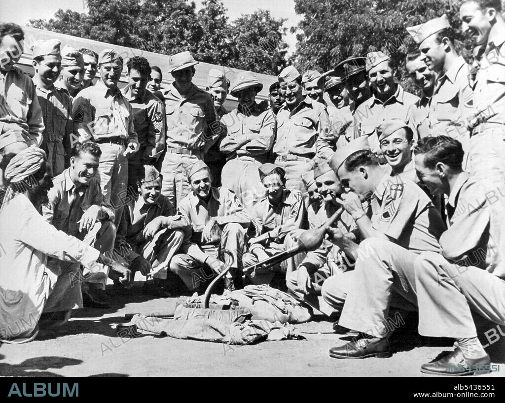 American Sergeant "Charms" Snake in India: To the amusement of his comrades stationed in India, a U.S. Army sergeant tries his skill at charming a hooded cobra snake with the pipe of the bonafide charmer squatting at left. March 8, 1943. (Photo by U.S. Office of War Information Picture).
