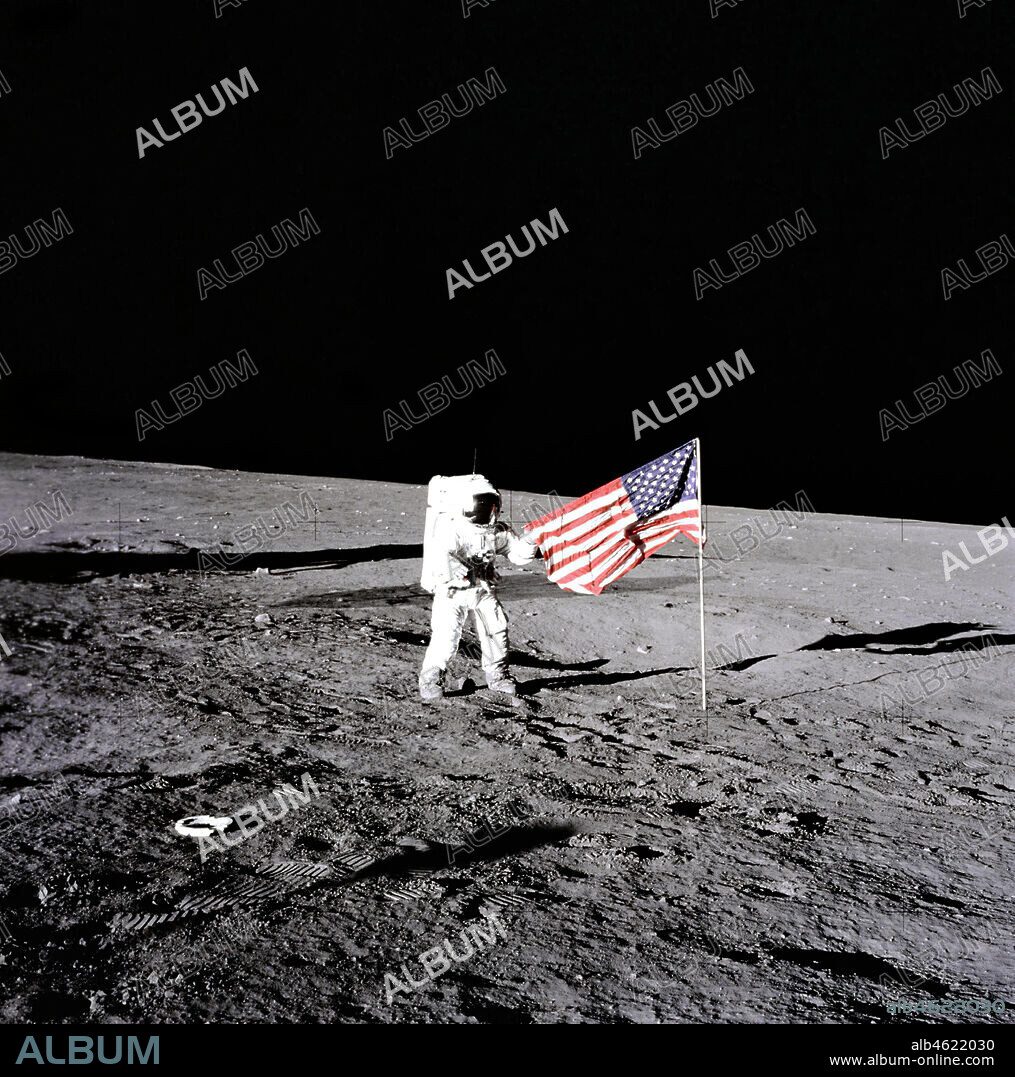 Apollo 12 - NASA, 1969. During the first extravehicular activity, astronaut Charles Conrad, Jr., Apollo 12 commander, releases the United States flag on the lunar surface. Boot prints from the astronauts can be seen in the image as well, November 19, 1969.