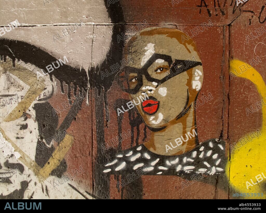 Pintura de cara de mujer joven en tonos marrones con gafas negras y labios pintados de rojo, graffiti, barrio Gòtic, Distrito Ciutat Vella, Barcelona en 2016.