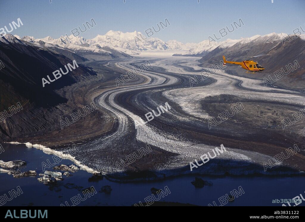 A helicopter flies over Lowell Glacier where it meets Lowell Lake in Kluane National Park, Yukon Territory, Canada.