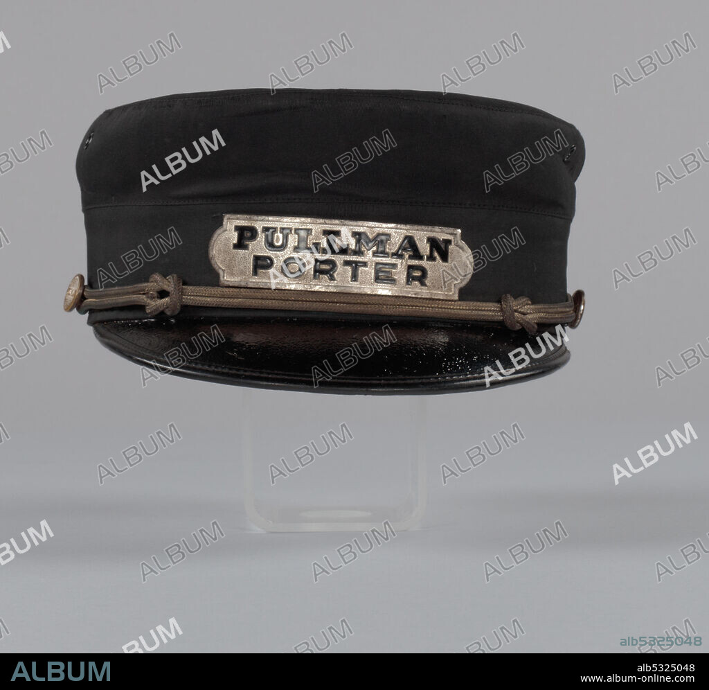 A Pullman Porter uniform cap owned by Robert Jackson Thomas. Being a Pullman porter was one of the jobs that helped build the black middle class in America, and Pullman porters were key figures in the civil-rights movement. The cap has a stiff, black crown and a black plastic visor. Metal buttons are on both sides of the cap where the visor meets the crown. The buttons are silver colored with the word “PULLMAN” on it. An off white corded strap connects both buttons and rests on the visor. A tarnished silver colored plate at the front of the cap has black lettering that reads “PULLMAN / PORTER.” Four black metal grommets are found in the top of the hat. The interior liner is a strip of brown leather sutured together at the seam.