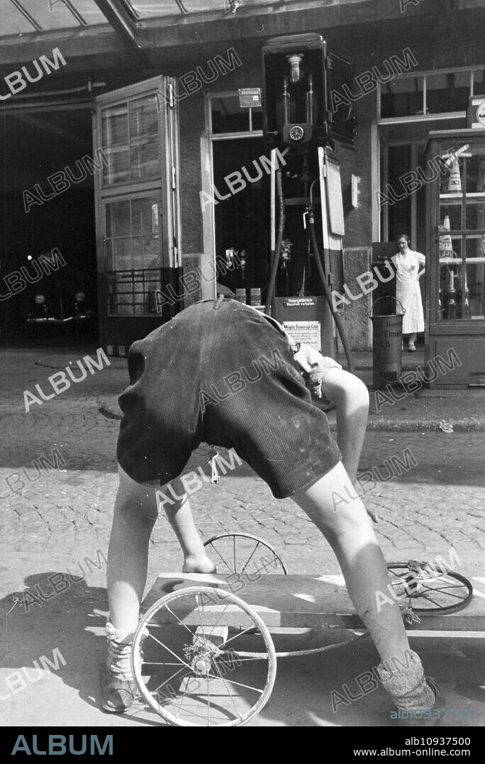 School boys oiling the wheels of their self-built wooden cart at a gas station, Stuttgart, Germany 1930s.