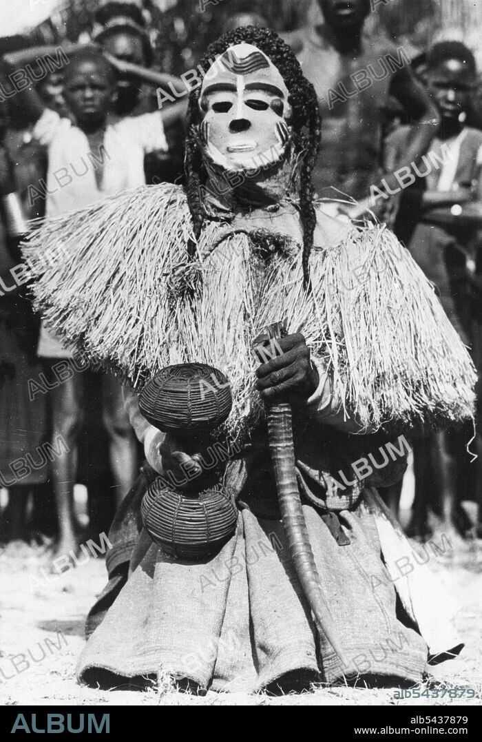 Congo Folklore -- One of the some twenty characters in the Mbuya dance of the Bapende tribe... An African Folklore 'play'. He wears a white-painted mask, Pigtails, and carries a basket filled with dried seeds and an Antelope horn. The Folklore of Africa lies, not in books, but in the Rhythmic Tribal dances that are handed down from generation to generation. the origins of the dance steps, the gestures and the sometimes fearful looking costumes are deep in the past, and deal with drought and rain.