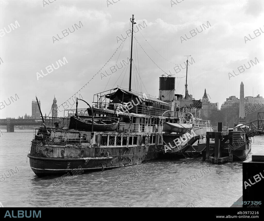 The Old Caledonia, derelict and fire damaged, moored on the Victoria Embankment, London, 1980. Landmarks visible in the background include Cleopatra's Needle, Big Ben and the Houses of Parliament.