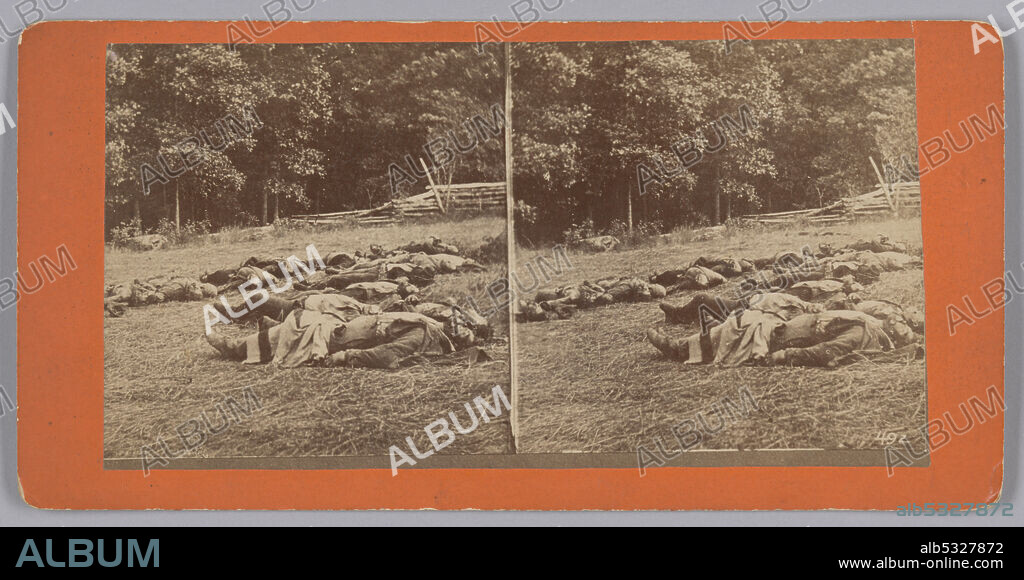 TIM O'SULLIVAN. This photographic print stereograph depicts the bodies of several deceased soldiers lying in an open field. A wooden fence in front of a dense forest of trees are in the background. The photographic print is mounted on orange cardboard that is pinkish on the reverse. A piece of paper adhered to the reverse of the mount has printed text with details of a series of Gettysburg battlefield photographs available from photographer and printer W. H. Tipton.