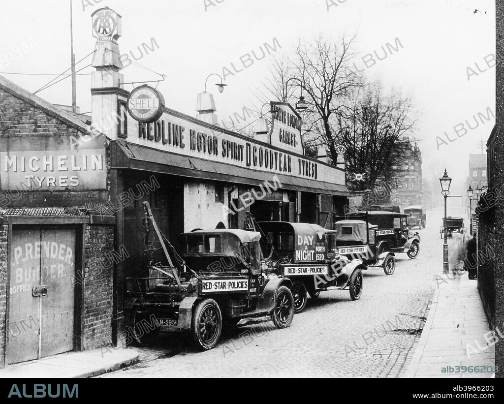 Daimler breakdown trucks, early 1920s. Two 1906/1908 Daimlers with chain drive chassis, converted into breakdown trucks. They offer day and night service and are parked outside a garage advertising tyres and motor spirit.
