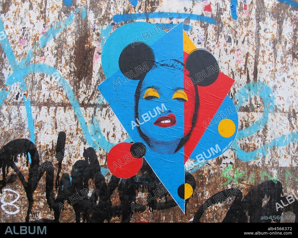 Pegatina del retrato de la cantante Madonna estilo pop art, con orejas de Mickey Mouse con fondo de triangulos y circulos rojos y azules, graffiti mural, barrio villa de gracia, Distrito de Gracia, Barcelona en 2016.