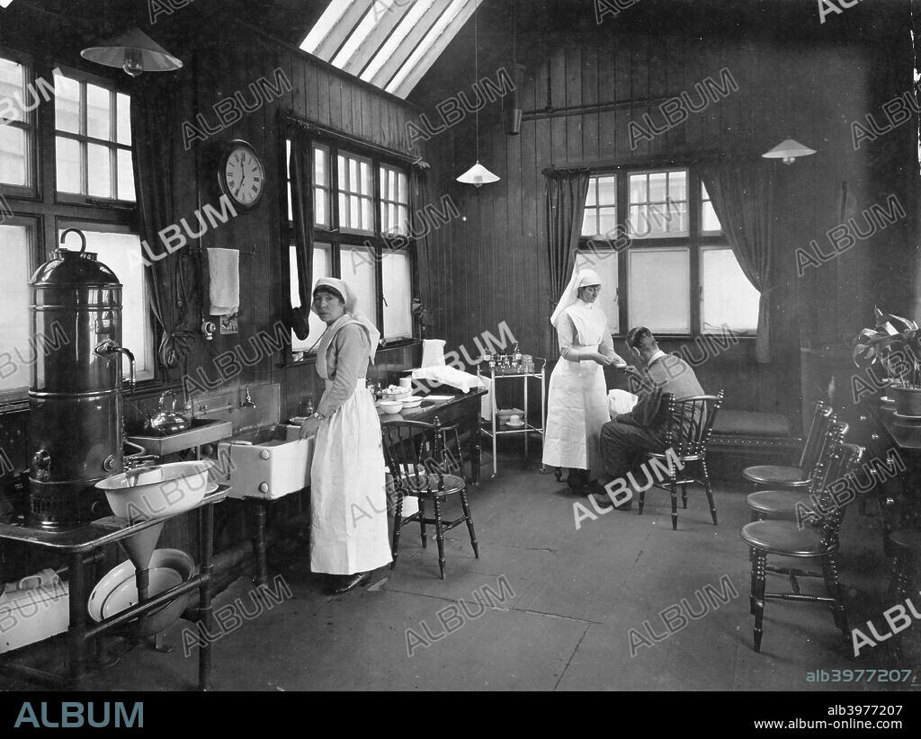 First aid room, Wolseley car factory, Birmingham, 1920s. Two nurses in a spacious-looking first aid room. One of them is treating a worker who has an injured hand.