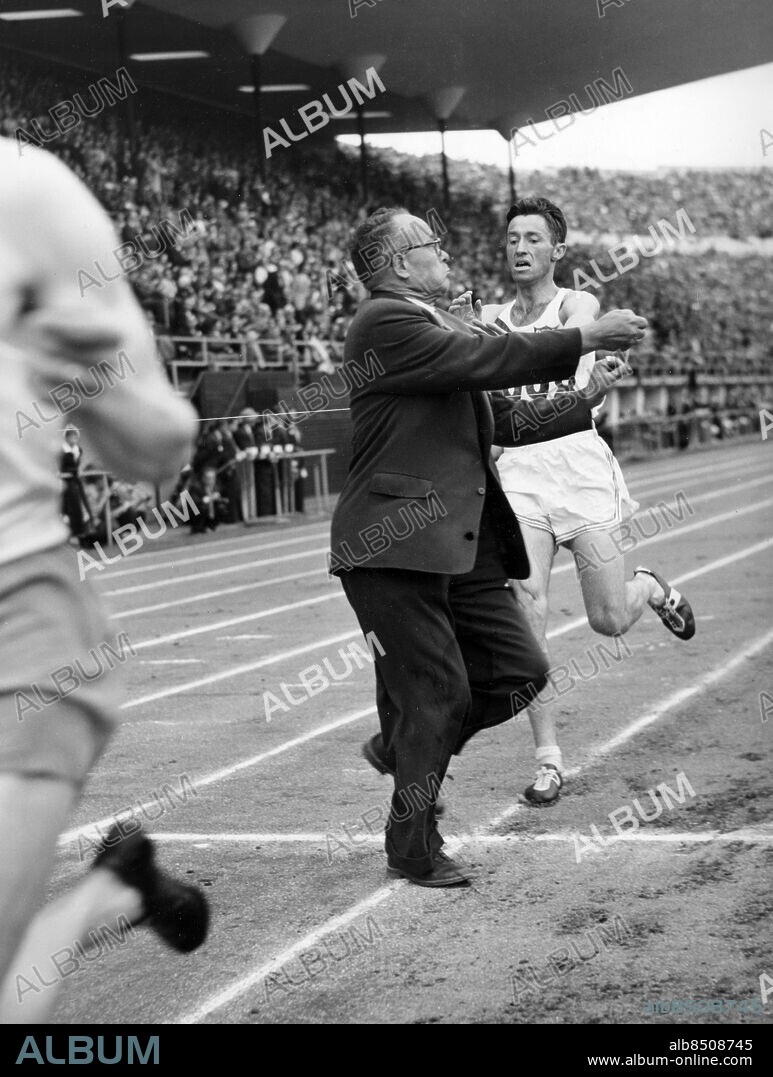FINLAND HELSINGFORS 1952-07-25.. En funktionär får skynda sig med målsnöret när Horace Ashenfelter (USA) springer i mål som segrare på 3000 m hinder vid de olympiska sommarspelen 1952 Till vänster ses en löpare som börjar på sitt sista varv.. Foto: Olympic World Photo Pool / AB Text & Bilder / SVT / Kod: 5600. Engelsk originalbildtext.. Mapp: Hinder (H-fors-oS 1952) I:586L. Hinderlöpning.