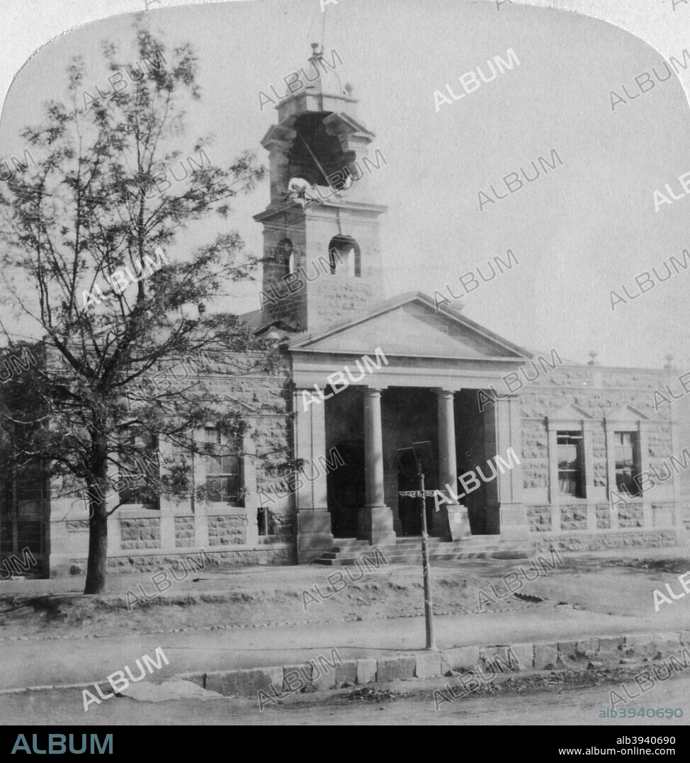The Town Hall, struck by a Boer shell during the siege, Ladysmith, South Africa, 1901. The siege of Ladysmith by the Boers lasted from 1 November, 1899 until 28 February, 1900. Some 20,000 soldiers and civilians were besieged in the town, a railway junction surrounded by hills. Shortages of food and fresh water, particularly after the Boers cut off the water supply to the town, caused around 60% of the casualties suffered by the defenders during the siege. Ladysmith was finally relieved after 118 days by a force commanded by General Redvers Buller, after two previous attempts had resulted in defeats at Colenso and Spion Kop. Stereoscopic card.