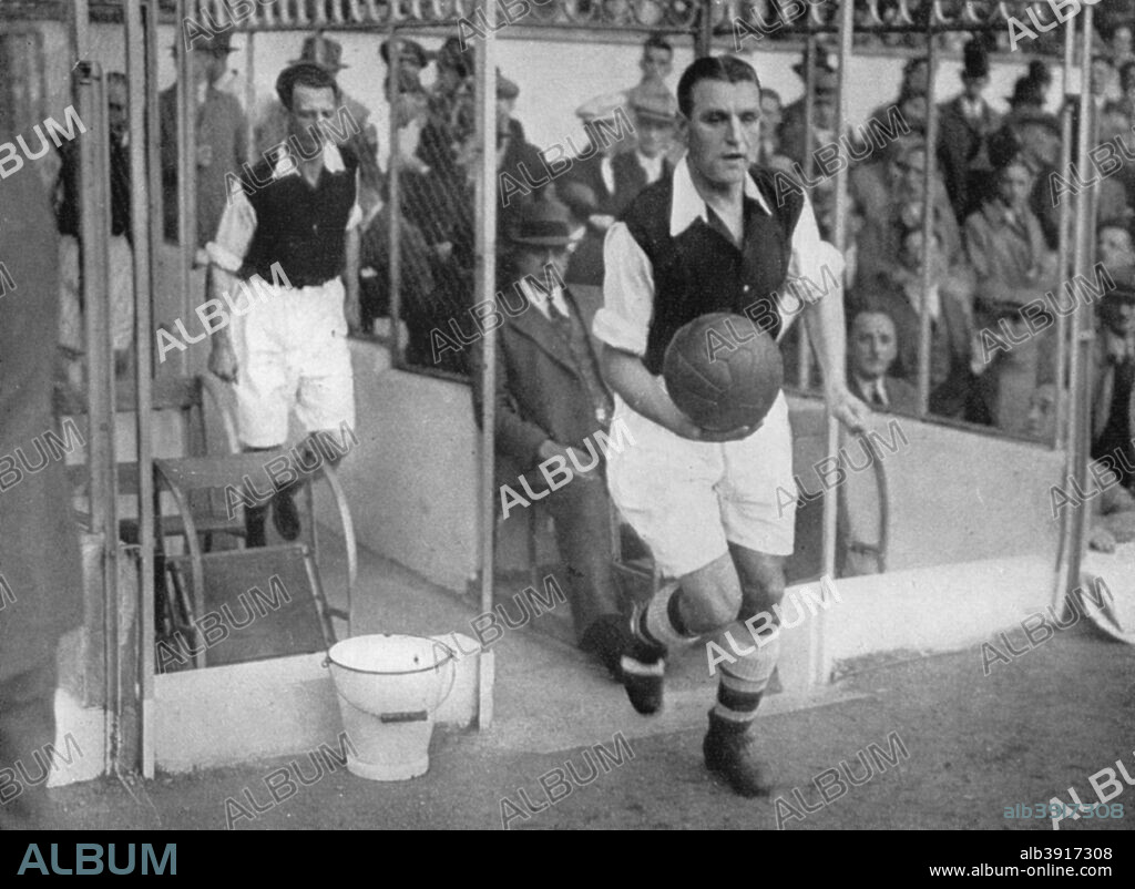 Arsenal FC captain Eddie Hapgood runs onto the pitch at Highbury, London, 1930s. A left back, Hapgood (1908-1973) was Arsenal's captain from 1933. In all he made 393 appearances for the club between 1927 and 1944 and also captained England in the 1930s. He is followed onto the field by centre half Herbie Roberts (1905-1944), who played 297 times for Arsenal between 1926 and 1937. A print from Football Ambassador by EA (Eddie) Hapgood, Sporting Handbooks LTD, London, 1945.