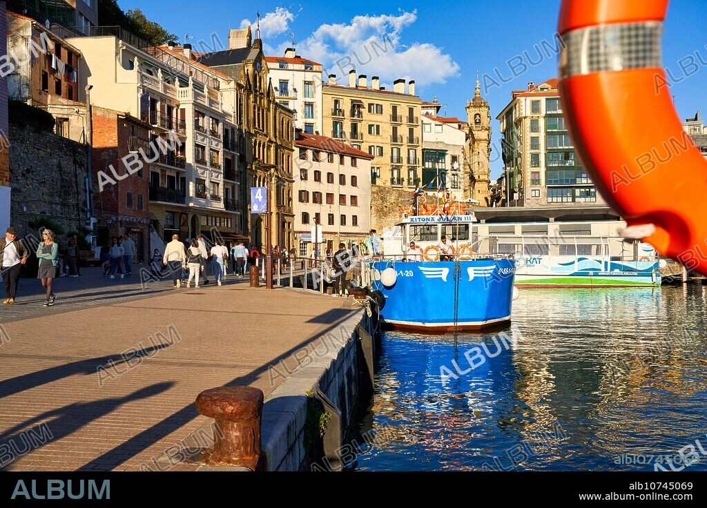 Barco turístico en el Puerto de Donostia, realiza excursiones por la Bahia de La Concha y la Isla Santa Clara, Al fondo Iglesia de Santa Maria y la Parte Vieja de la ciudad, Donostia, San Sebastian, Basque Country, Spain, Europe.