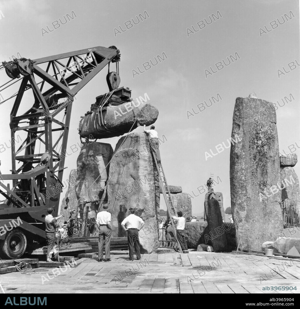Re-erection of Trilithon lintel, Stonehenge, Wiltshire, 1958. Re-erection of Trilithon lintel 158 by the 60 ton 'Brabazon Crane', the larger of two cranes used to lift stones. The lintel is being lowered and man-handled into its final resting position on upright stones 57 and 58. Photographed by R J C Atkinson, January 1958.