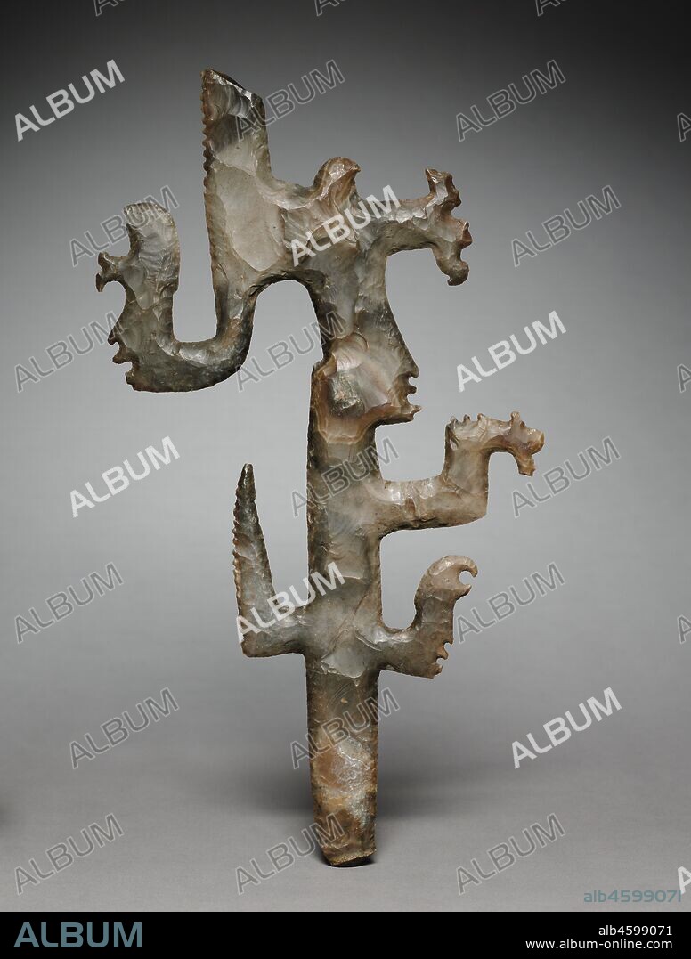 Eccentric Flint, 600-900. Named for their unusual shapes, eccentric flints often have intricately silhouetted figures like this. At the forehead of the main profile face is a smoking torch, the insignia of a deity closely linked to rulers and known today as K?awil. Smaller faces appear on three protrusions. Some flints may have served as scepters; they also were buried as offerings beneath buildings and sculptures.