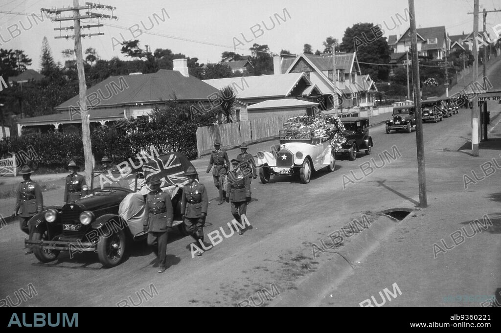 Funeral Procession, Unknown, circa 1930, black-and-white photography, View of a cortege showing a group of uniformed soldiers escorting a hearse which is carrying a coffin draped with a Union Jack. The hearse is being followed by a long procession of motorcars.