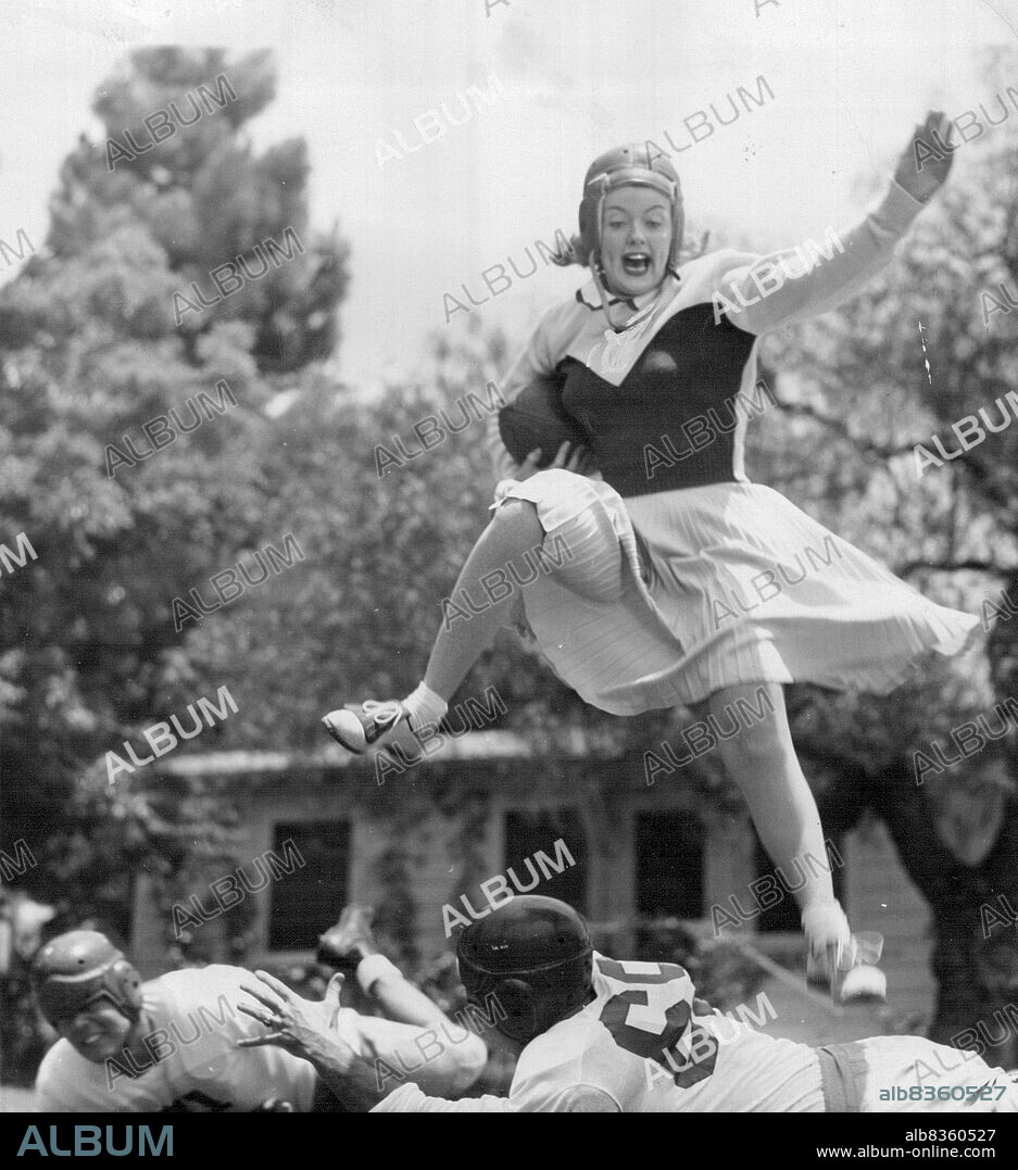A Jump Ahead Of The Game -- High-jumping Martha Stewart, film actress and former cheer leader and drum Majorette at the University of California at Los Angeles, "Hurdles The Line" to remind us that the football season will soon be upon us. The players are star backs from U.C.L.A. and Texas Christian. Martha is working in the film, "I Wonder Who's kissing her now, her third picture. August 17, 1946. (Photo by Wide World Photos).