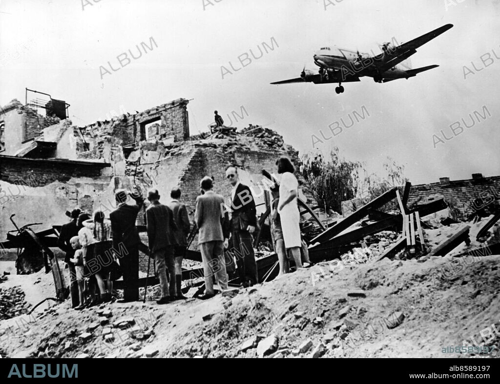 Orig. bildtext... A.O.A. CARRIES ITS 5.000.000th POUND IN BERLIN AIRLIFT. A loaded C-54, a unit of the US air plane which are transporting supplies for 2,400,000 of Berlin's population flies over the ruins of one section of the city as it approaches Tempelhof air base. Berlin residents are shown watching the big food-carrier as it nears the field. Anm. Berlinblockaden 1948-49 Efterkrigstiden Blockader Hjälpsändningar Bildarkivets katalog 52:2 sites: TYSKLAND;USA*;BERLIN.