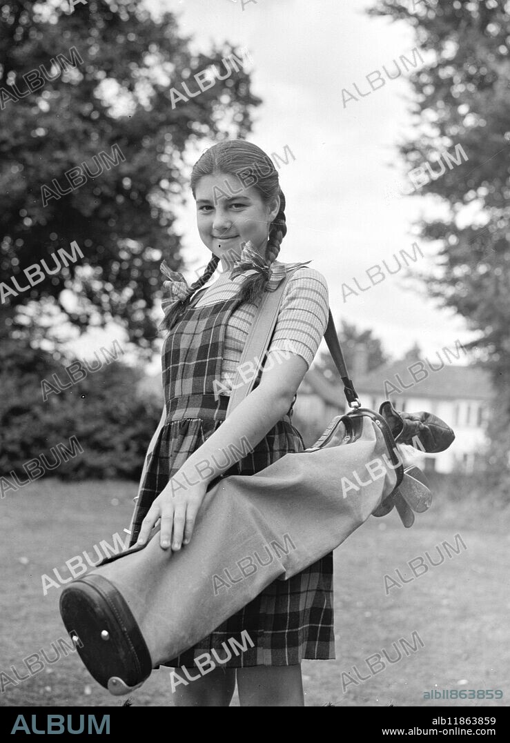 YOUNG COMPETITOR IN GOLF CHAMPIONSHIP. Girl wearing a smile as she shoulders her golf clubs is Dolores Windsor, daughter of the Ruislip (Middlesex) club professional, who at 12 years of age is the youngest entrant for the girls open golf championship to be held at Beacons field (Bucks.) on September 7-9. Dolores she is pictured at Ruislip golf club where she is practising for the big event -has been playing golf since she was 7, this is her first appearance in the competition. 12 September 1949.