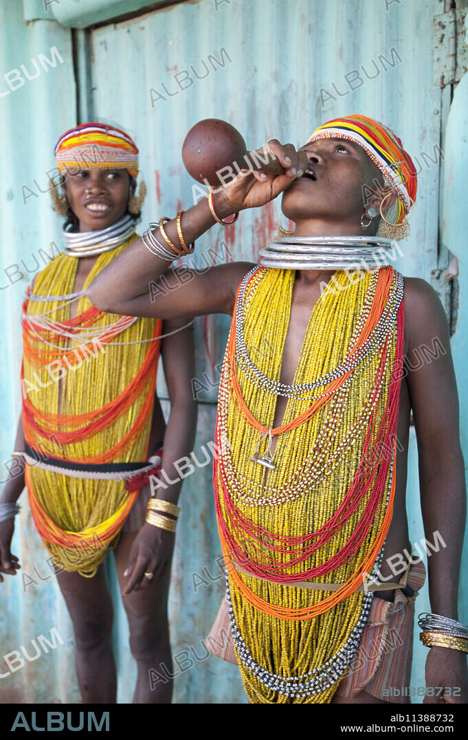 Two Bonda tribeswomen wearing traditional beads with beaded caps and metal necklaces drinking village alcohol from gourd vessel, Rayagader, Orissa, India, Asia.