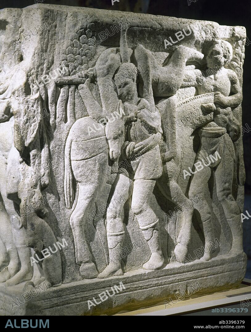 "Sarcófago de Hipólito". Detalle del altorrelieve de uno de los costados cortos del mismo. En éste comienza el relato del mito, Hipólito llegando de su partida de caza. Dos sirvientes descargan del lomo de un burro el ciervo cazado. Fechado en el siglo III d. C. Procede de Tarraco. Museo Nacional Arqueológico. Tarragona. Cataluña.