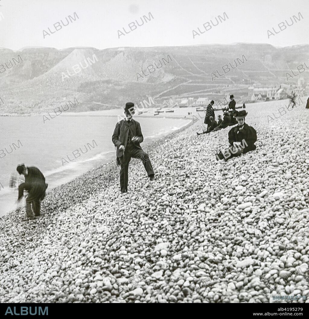 Magic lantern slide circa 1900.Victorian/Edwardian.Social History.Chesil Beach , sometimes called Chesil Bank, in Dorset, southern England is one of three major shingle structures in Britain.[1] Its toponym is derived from the Old English ceosel or cisel, meaning 'gravel' or 'shingle' The beach is often identified as a tombolo, although research into the geomorphology of the area has revealed that it is in fact a barrier beach which has 'rolled' landwards, joining the mainland with the Isle of Portland, giving the appearance of a tombolo.[2] The shingle beach is 29 kilometres (18 mi) long, 200 metres (660 ft) wide and 15 metres (50 ft) high. The beach and The Fleet, a shallow tidal lagoon,[3] are part of the Jurassic Coast, a UNESCO World Heritage Site, and the location for a 2007 novel, On Chesil Beach by Ian McEwan.